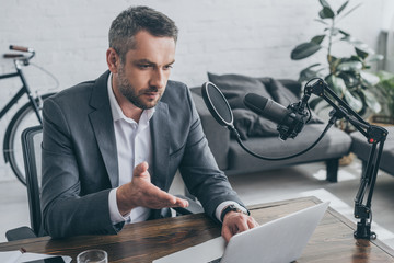 handsome radio host using laptop while sitting at workplace near microphone