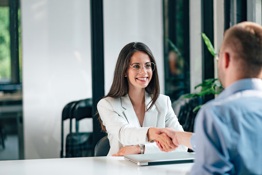 Positive young businesswoman handshake with a businessman while sitting at the office desk.