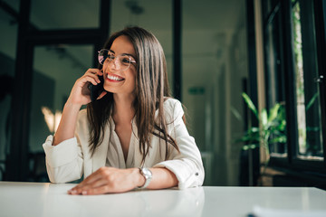 Portrait of a elegant positive businesswoman talking on smart phone at modern office. - Powered by Adobe