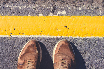 A person is standing next to the yellow line drawn. Shoes stoin on the pavement gray shade.