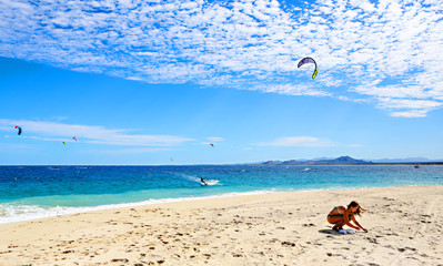A young woman on the beach with kite surfers behind her in the water. 