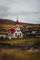 Sandavagur Church / Sandavags Kirkja during moody spring evening with glowing red roof situated in the picturesque village Sandavagur (Faroe Islands, Denmark, Europe)