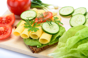 Making healthy eating concept - fresh and multi colored sandwich with dark wholemeal bread and cheese, lettuce, tomato, cucumber, dill, young onion on wooden board in close-up