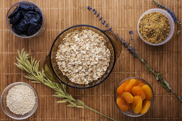 oat flakes with dried apricots  seeds flax and sesame and prunes stand on a wooden tray with wildflowers