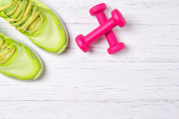 Fototapeta na wymiar Fitness concept, green sneakers and pink dumbbells on wooden background, top view with copy space