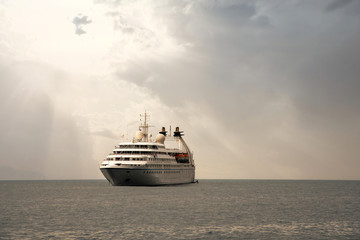 Fototapeta na wymiar A luxury cruise ship anchored offshore with sun rays filtering through clouds, Portofino, Genoa, Liguria, Italy