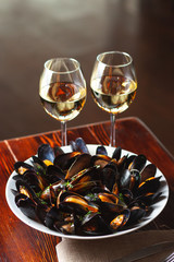 Fine dining in a seafood restaurant: a big dish of mussels with bottle of white wine with two wine glasses, on dark background