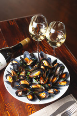 Fine dining in a seafood restaurant: a big dish of mussels with bottle of white wine with two wine glasses, on dark background