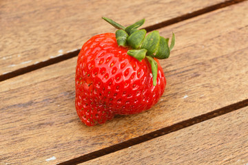 One strawberry with leaves on a wooden table