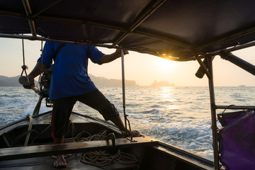 A local man sails on a Thai long-tail boat, driving it into the sea in the morning at dawn. View from inside the boat