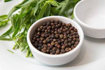 Black pepper in white bowl over white background . Saucer dish with black pepper peas isolated on white background . Dry black peppers isolated with path .