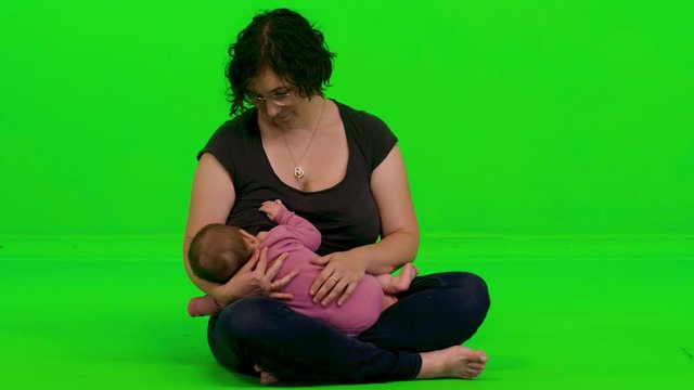Young beautiful mother breastfeeding her baby girl over a green screen.