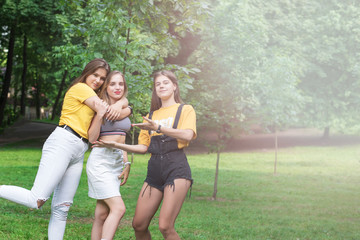 Obraz premium Three nice teen girls having fun in the park. Excellent sunny weather. Summer concept. Hugging. Lifestyle. Trendy Hipster Girls