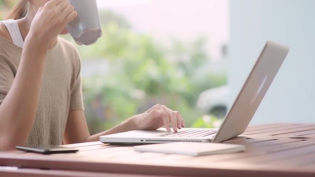Freelance Asian woman working at home, business female working on laptop and drinking coffee sitting on table in the garden in morning. Lifestyle women working at home concept.