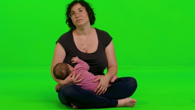 Young beautiful mother breastfeeding her baby girl over a green screen.