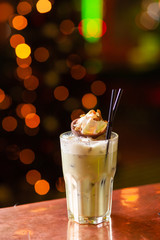 Iced latte matcha alcoholic cocktail on a light wooden bar counter with bokeh background
