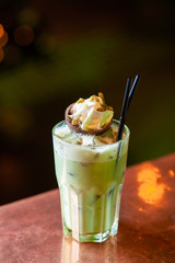 Iced latte matcha alcoholic cocktail on a light wooden bar counter with bokeh background