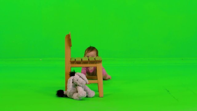 A baby girl crawls, stands using a chair, laughs happily and cheerfully over a green screen.