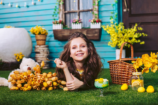 Funny happy girl with wavy curls lies on a green lawn and laughs, holding a teaspoon in his hand for ice cream. Easter celebration. - Powered by Adobe