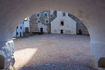 An arch in a thick stone fortress wall leads to the inner paved courtyard of the medieval historic Abo castle in the city of Turku in Finland on a sunny summer day.