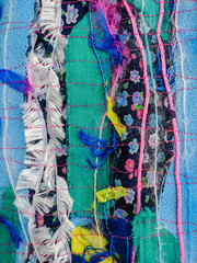 Colourful torn fabric strips, cords and wool, sewn together in a striped pattern. Textile art textured background. Vertical.