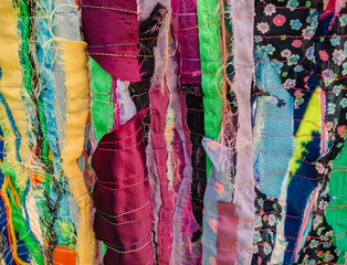 Colourful torn fabric strips, cords and wool, sewn together in a striped pattern. Textile art textured background.