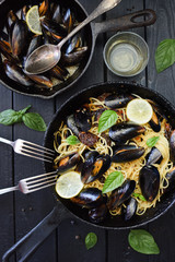 Seafood pasta. Delicious spaghetti with mussels, basil, lemon and white wine in cast iron pans on black background