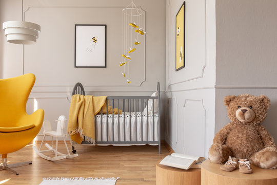 Teddy bear, crib and yellow armchair in a toddler room interior. Real photo