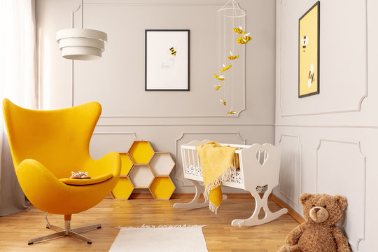 Yellow armchair, honeycombs and crib in a toddler room interior. Real photo