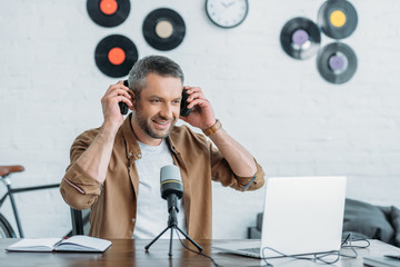 handsome radio host looking at laptop while sitting at workplace and putting on headphones