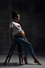 Beautiful young pregnant happy mother woman in white t-shirt posing on dark 