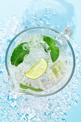 A big jug with a mojito cocktail on a light blue background. The concept of soft drinks in the summer heat.