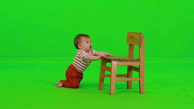 Laughing happily while standing using a chair by a cute baby girl over a green screen.
