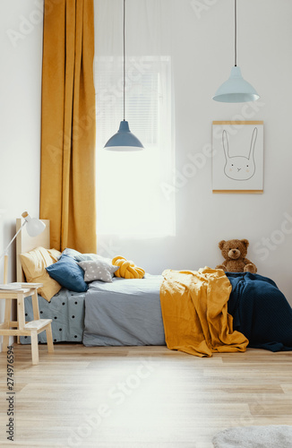 Teddy bear on single wooden bed in blue and orange bedroom interior
