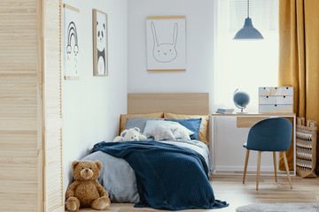 Desk, chair and single bed with blue bedding in cozy bedroom interior for children
