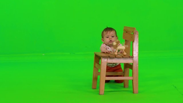 Adorable baby stands and play with a toy happily, chewing it and trying to pick it up, over a green screen.