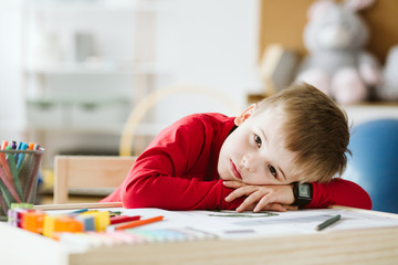 Sad little boy in red sweater feeling lonely and lying on a table