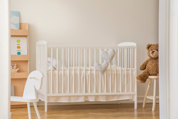 Teddy bear, rocking horse and white wooden crib with heart shaped pillows in scandinavian design...