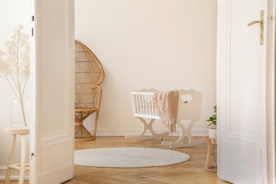 White open double door in elegant apartment with nursery designed with white crib and wicker peacock chair, real photo with copy space