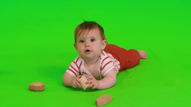Beautiful baby girl smiles and plays happily with wooden toys over a green screen.