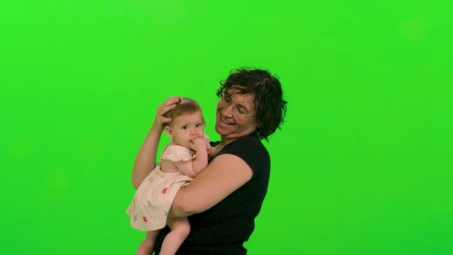Young mother holds and hug her sleepy baby girl over a green screen.