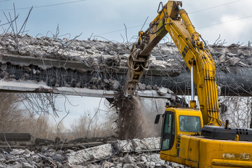 Professional demolition of reinforced concrete structures using industrial hydraulic hammer. Rods of metal fittings. Wreckage and crumbles of concrete.