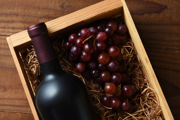 A high angle closeup of a red wine bottle in a wood crate with grapes.