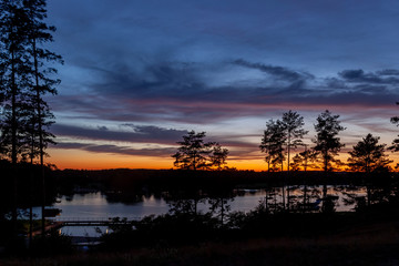 Piękny zachód słońca nad jeziorem Kalwa na Mazurach w Polsce., na pierwszym planie kontury drzew.