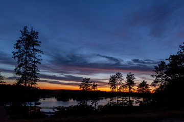 Fototapeta na wymiar Piękny zachód słońca nad jeziorem Kalwa na Mazurach w Polsce., na pierwszym planie kontury drzew.