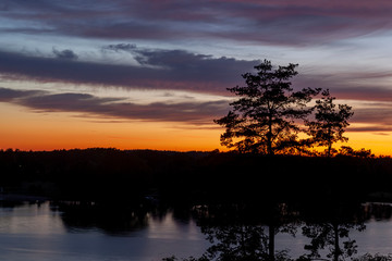 Piękny zachód słońca nad jeziorem Kalwa na Mazurach w Polsce., na pierwszym planie kontury drzew. - obrazy, fototapety, plakaty