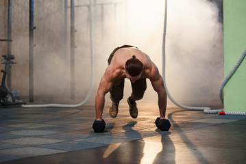 Young strong man doing pushups with dumbbells during training in the gym.