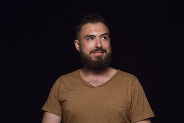 Obraz premium Close up portrait of young man isolated on black studio background. Photoshot of real emotions of male model. Dreaming and smiling, hopeful and happy. Facial expression, human emotions concept.