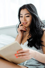 selective focus of attractive thai woman reading book and touching face