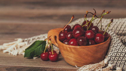 Fresh cherries with green leaves in wooden bowl, close up